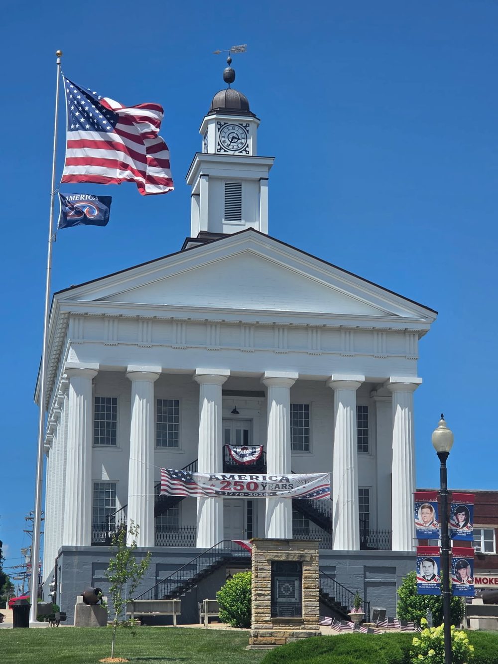 The historic Orange County Courthouse on the square in Paoli, Indiana, flying American flags beneath an America 250 banner.